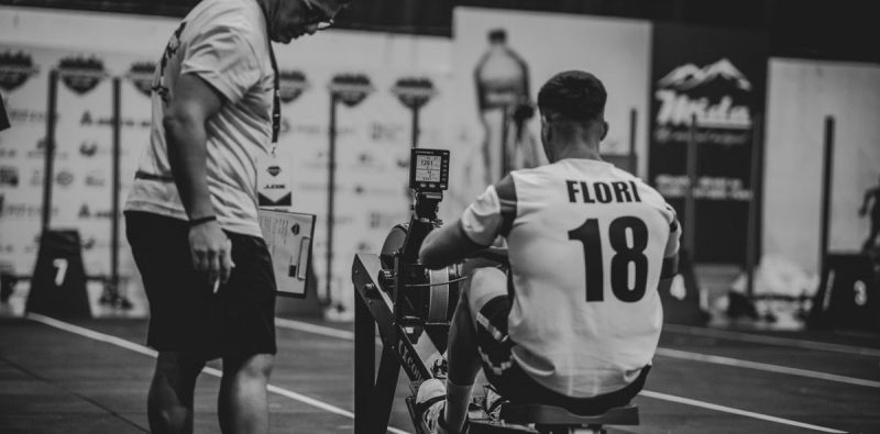 An athlete using a rowing machine indoors, coached in a gym setting.